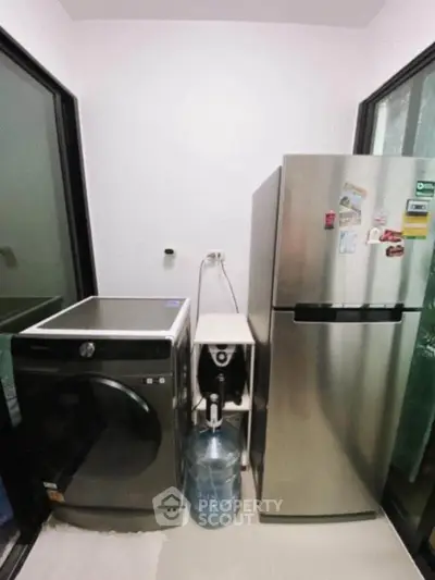Modern laundry area with washing machine and stainless steel fridge in compact space.