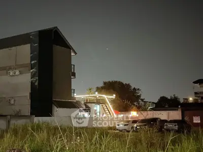 Night view of modern building with parking area and illuminated rooftop.