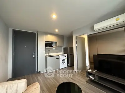 Modern living room with integrated kitchen and washing machine, featuring sleek design and neutral tones.