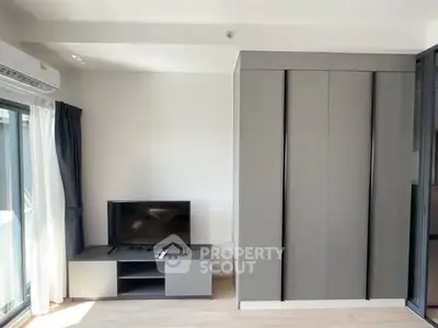 Modern living room with sleek TV stand and large wardrobe, featuring natural light from a window.