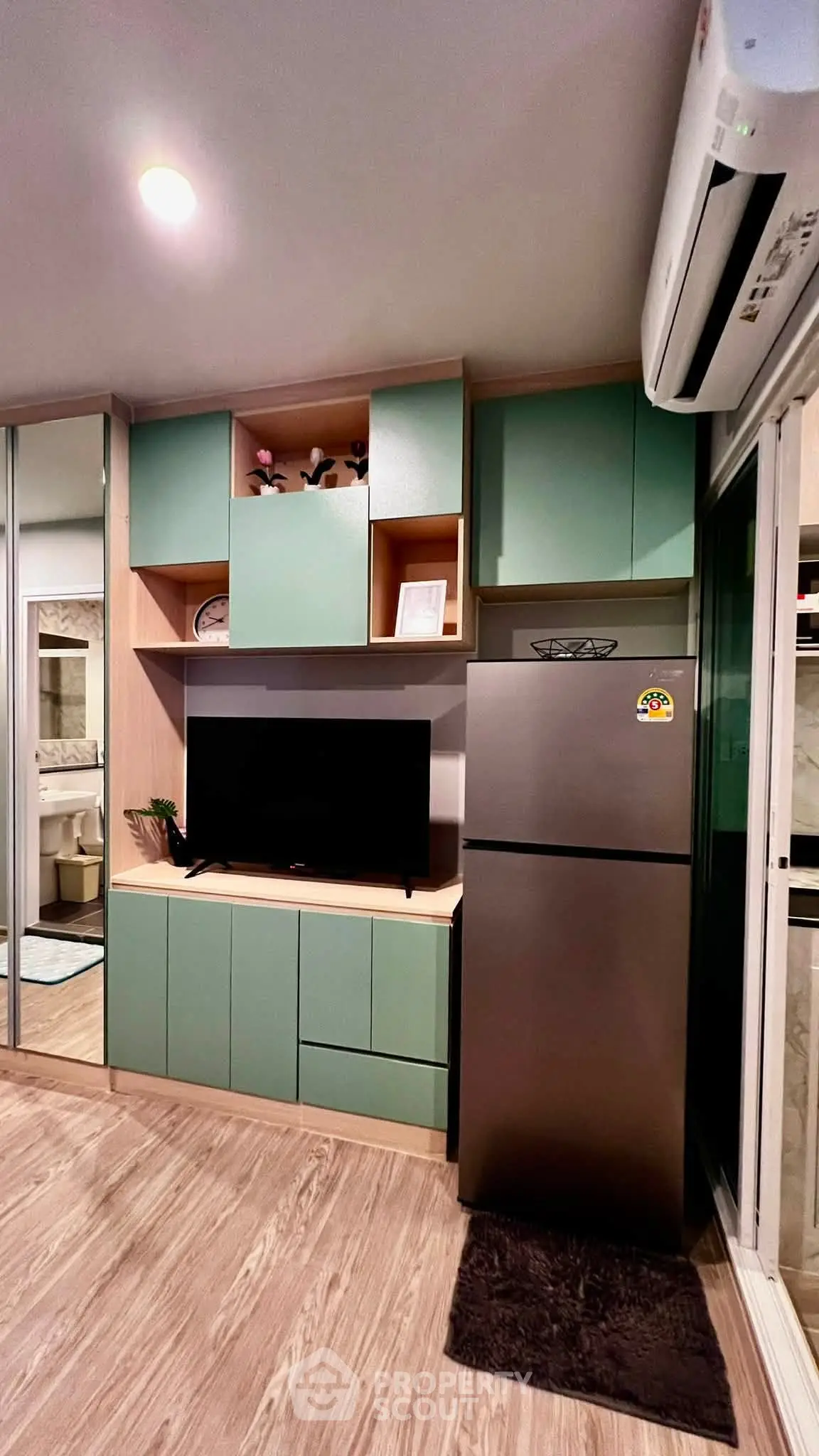 Modern living room with sleek cabinetry and stainless steel fridge, featuring stylish decor and air conditioning.