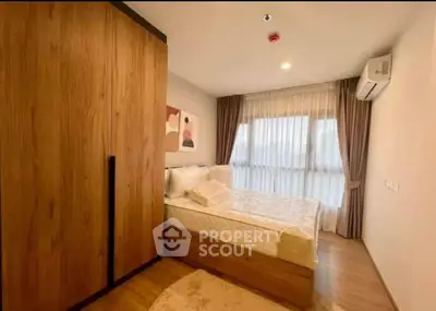 Cozy bedroom with wooden wardrobe and large window, perfect for relaxation.