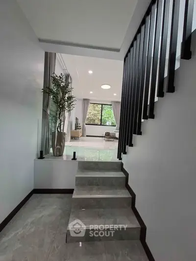 Modern interior staircase leading to a bright living room with large windows and elegant decor.
