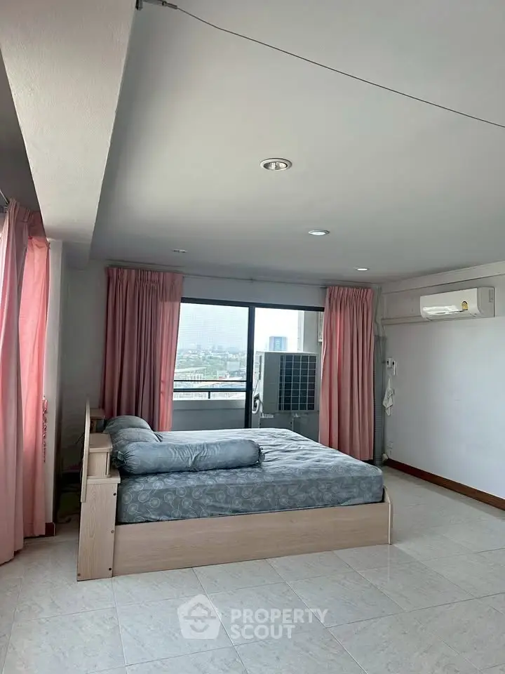Spacious bedroom with large windows and city view, featuring modern furnishings and natural light.
