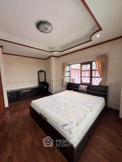 Spacious bedroom with elegant wooden flooring and large window for natural light.