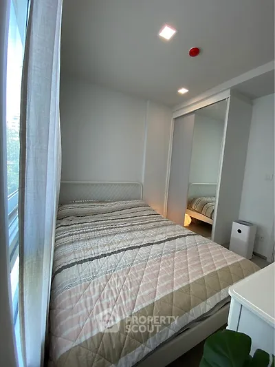 Cozy bedroom with modern decor and ample natural light from large window.
