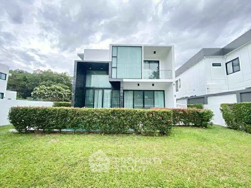Modern two-story house with large windows and lush green lawn, perfect for contemporary living.
