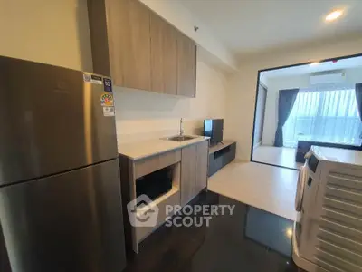 Modern apartment kitchen with sleek appliances and open layout, leading to a bright living area with large windows.