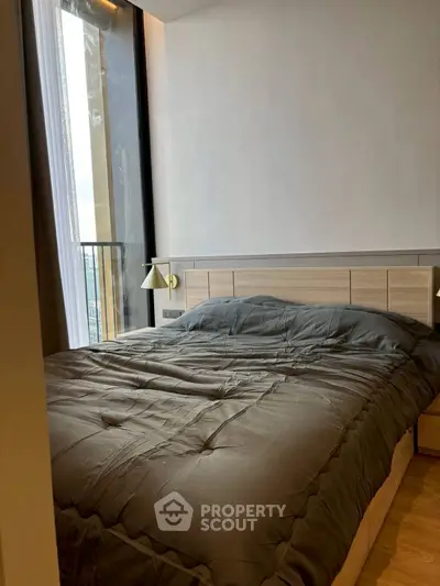 Modern bedroom with large window and stylish decor in urban apartment.