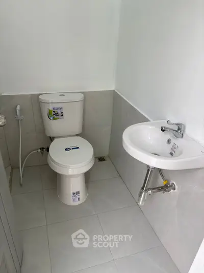 Compact bathroom with modern fixtures and white tiles, featuring a toilet and small sink.