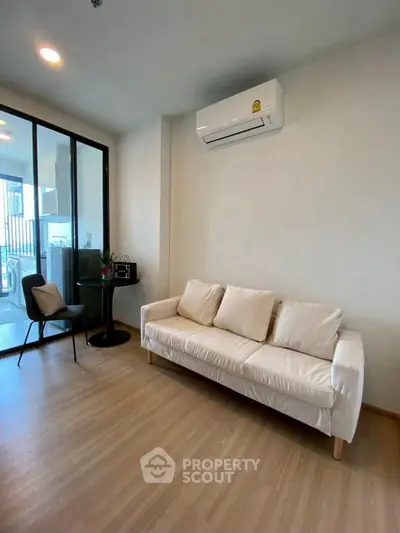 Modern living room with white sofa and air conditioning, featuring a sleek glass door to balcony.