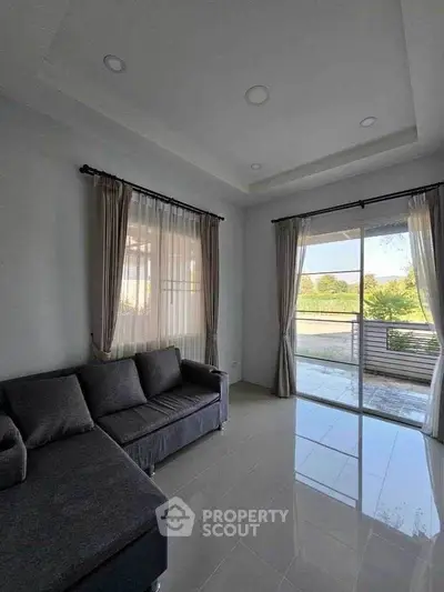 Spacious living room with modern sofa and large window opening to a scenic balcony view.