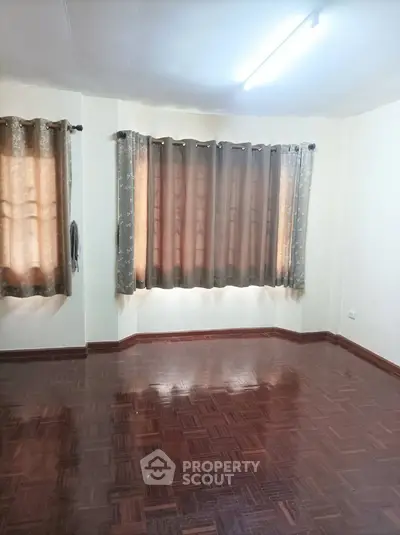 Spacious and well-lit living room with polished parquet flooring and elegant curtains, perfect for comfortable urban living.