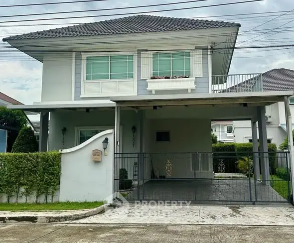 Charming two-story house with gated driveway and lush greenery in a serene neighborhood.