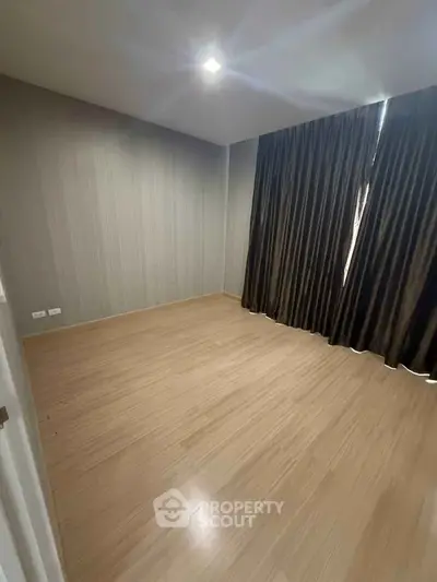 Spacious empty room with wooden flooring and elegant dark curtains, perfect for customization.