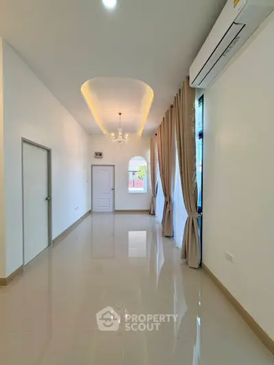 Elegant living room with high ceiling and chandelier, featuring large windows and modern air conditioning.