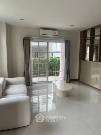 Spacious living room with modern sofa and large window overlooking garden, perfect for relaxation.