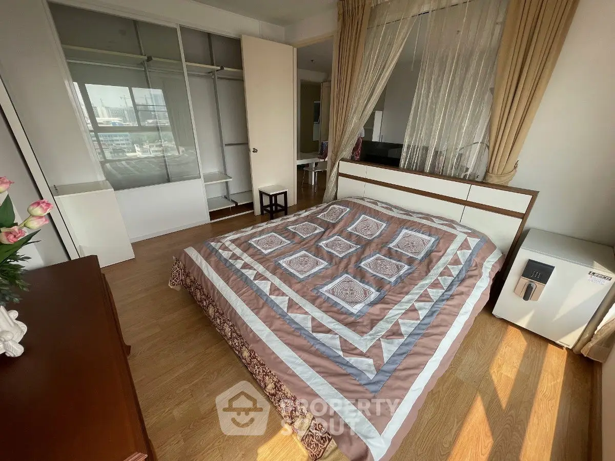 Spacious bedroom with wooden flooring and ample natural light, featuring a cozy bed and open wardrobe.