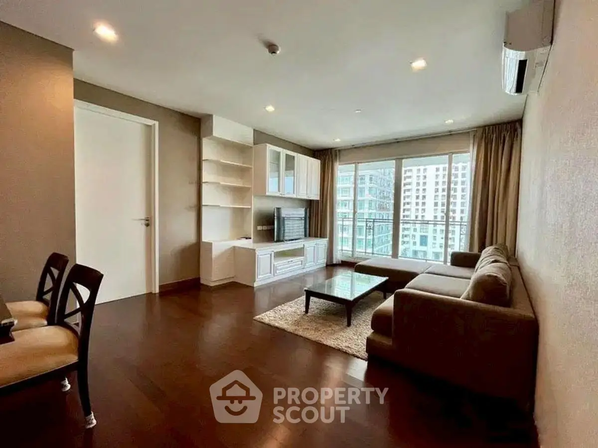 Spacious modern living room with large windows and city view, featuring elegant furniture and hardwood floors.