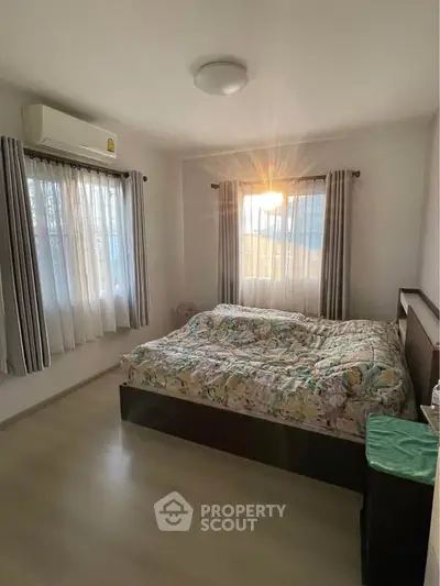 Cozy bedroom with natural light and air conditioning, featuring a comfortable bed and stylish curtains.