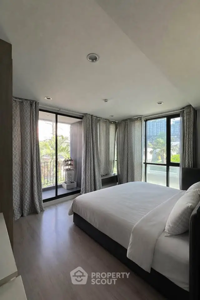 Spacious bedroom with large windows and balcony access in modern apartment.