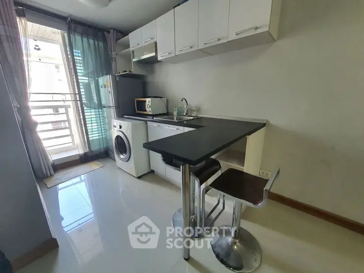 Modern compact kitchen with washing machine and breakfast bar in bright apartment.