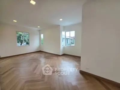 Spacious living room with elegant herringbone wood flooring and large windows offering natural light.