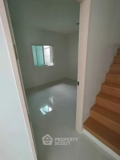 Spacious room with glossy white tiles and wooden staircase, perfect for modern living.