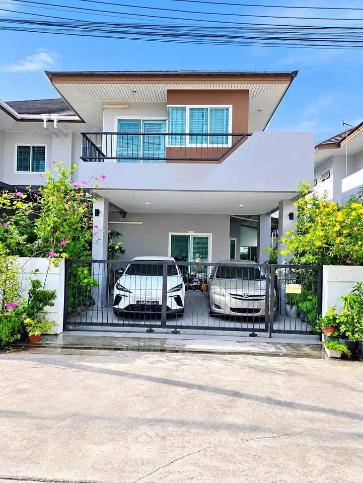 Modern two-story house with two cars parked in the driveway, surrounded by lush greenery.