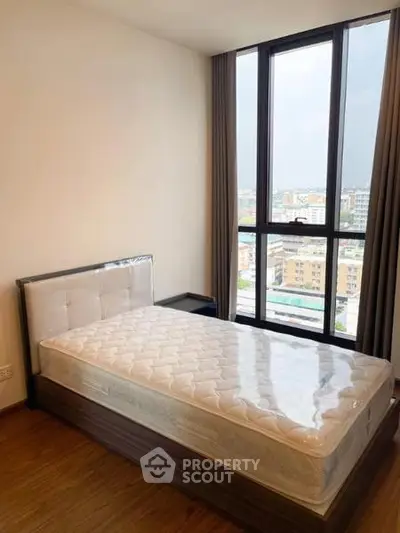 Modern bedroom with large window and city view, featuring a comfortable bed and wooden flooring.
