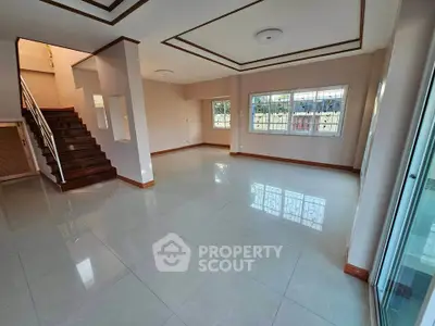 Spacious living room with large windows and elegant staircase in modern home.