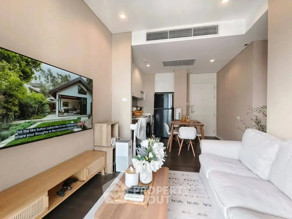 Modern living room with cozy seating and large TV, open to dining area and kitchen with sleek appliances.