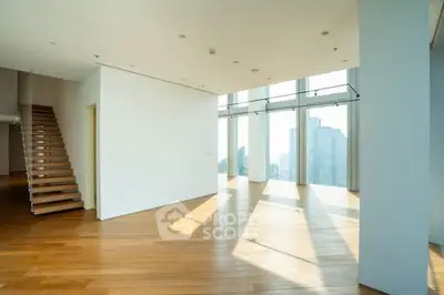 Spacious modern living room with floor-to-ceiling windows and wooden flooring, offering abundant natural light.