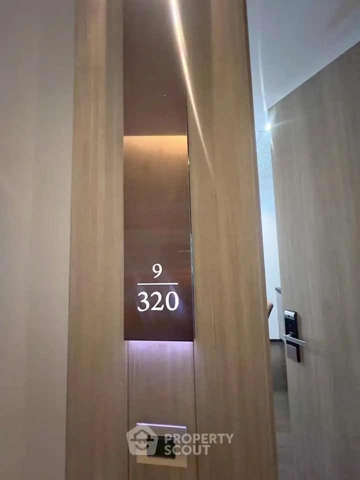 Modern apartment entrance with sleek wooden door and illuminated room number 320, showcasing contemporary design.