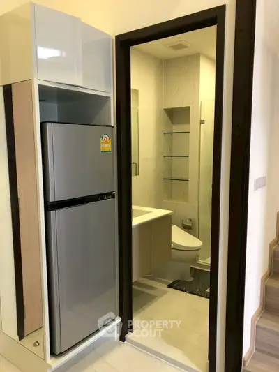Compact modern bathroom with adjacent stainless steel fridge in a cozy apartment setting.
