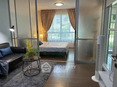 Modern studio apartment with cozy living area and bedroom separated by glass partition.