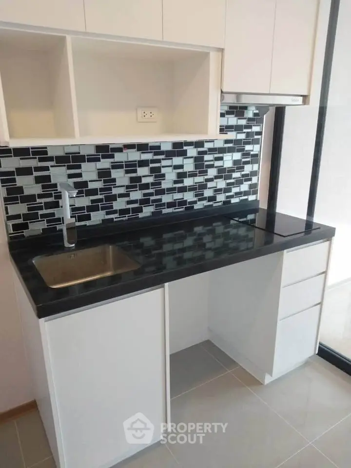 Modern kitchen with sleek black countertop and stylish backsplash in a contemporary apartment.