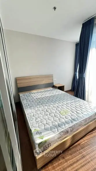 Modern bedroom with wooden flooring and large window with blue curtains
