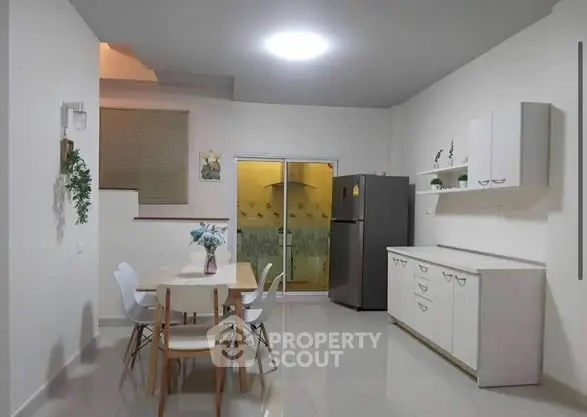 Modern kitchen with dining area, sleek white cabinets, and stainless steel fridge in a cozy apartment.