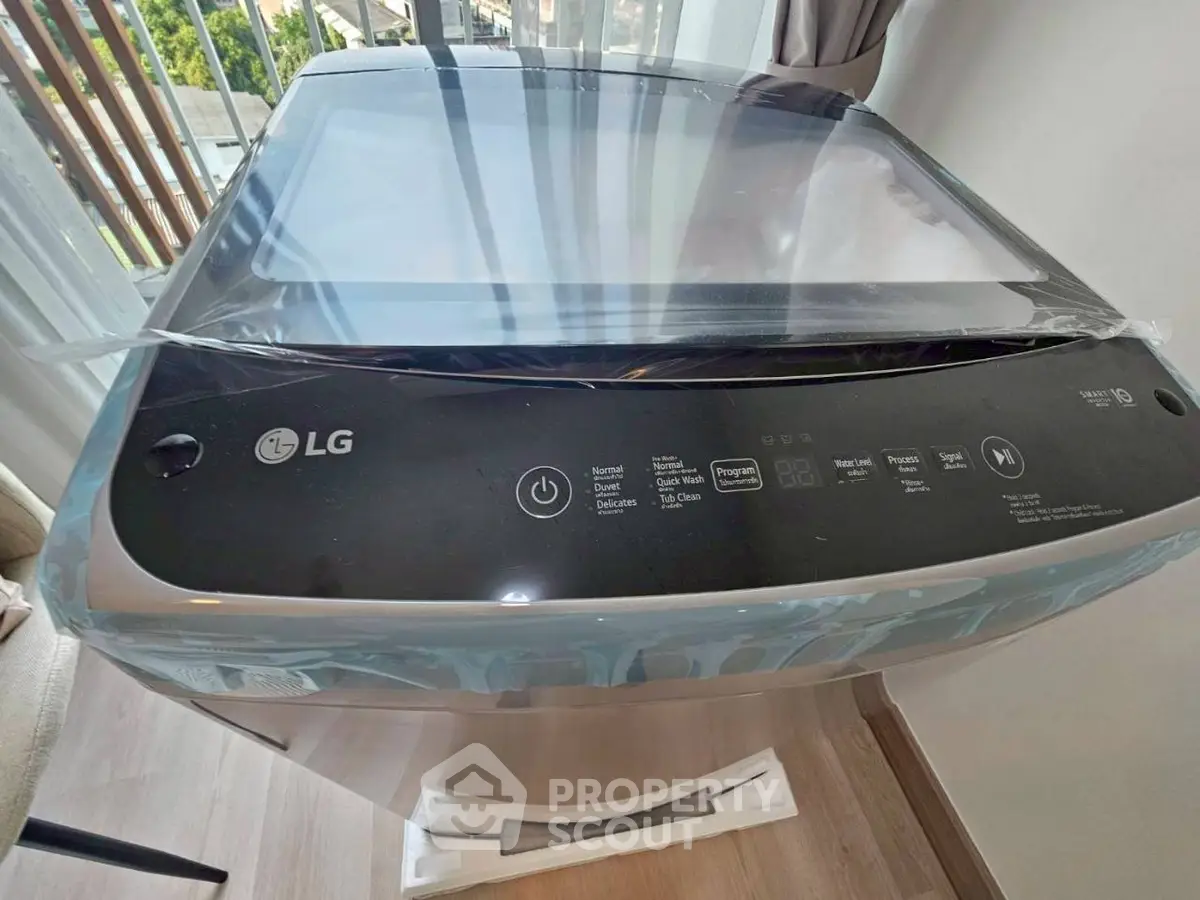 Modern washing machine in a bright laundry area with large windows and wooden flooring.