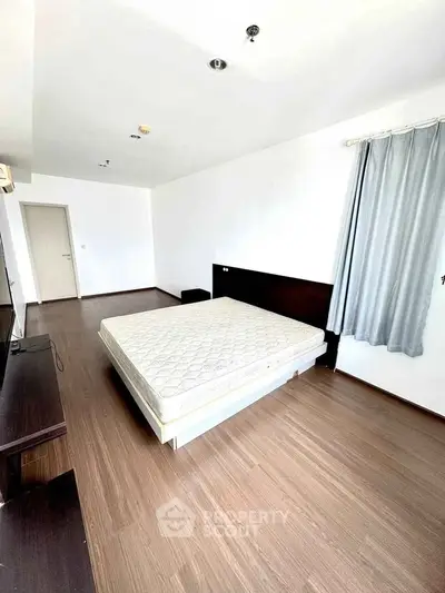 Spacious bedroom with wooden flooring and large window for natural light.