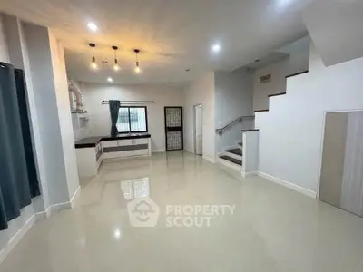 Spacious modern living room with elegant lighting and staircase, perfect for family gatherings.