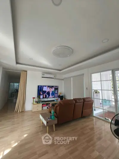 Spacious living room with modern decor and large TV, featuring natural light and wooden flooring.