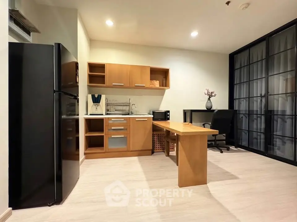 Modern kitchen with sleek black fridge and wooden cabinetry in a stylish apartment.