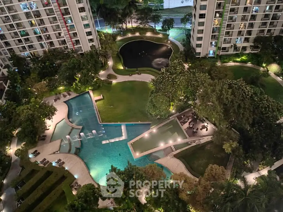 Luxurious residential complex with illuminated pool and lush gardens at night.