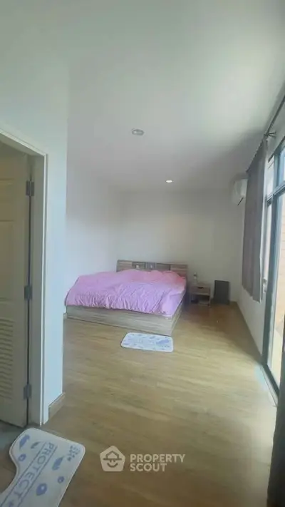 Spacious bedroom with wooden flooring and large window for natural light