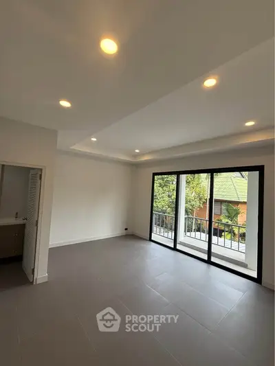 Spacious living room with large windows and balcony view, modern lighting, and sleek tile flooring.