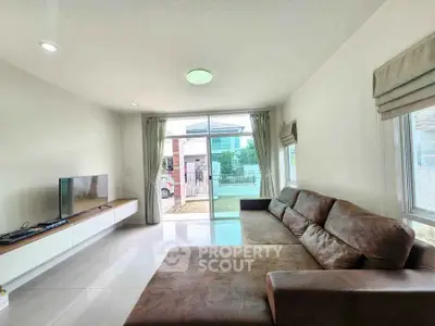 Spacious living room with large sofa and modern TV setup, featuring natural light from sliding glass doors.
