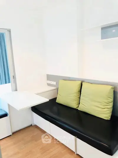 Modern minimalist living room with sleek black sofa and green cushions, featuring a compact foldable table.