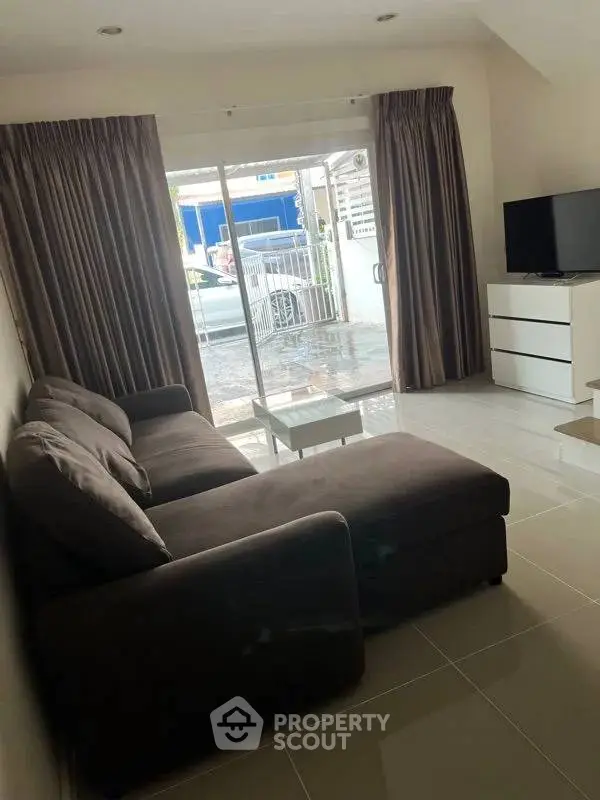 Cozy living room with modern sofa and TV, sliding glass doors open to a bright exterior view.